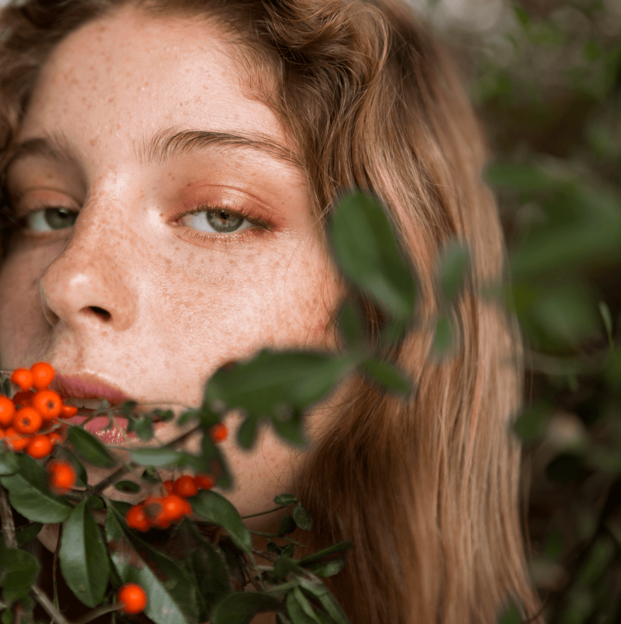 Close-up of a young person with natural skin and freckles holding green branches with orange berries, representing skincare for youth and children.