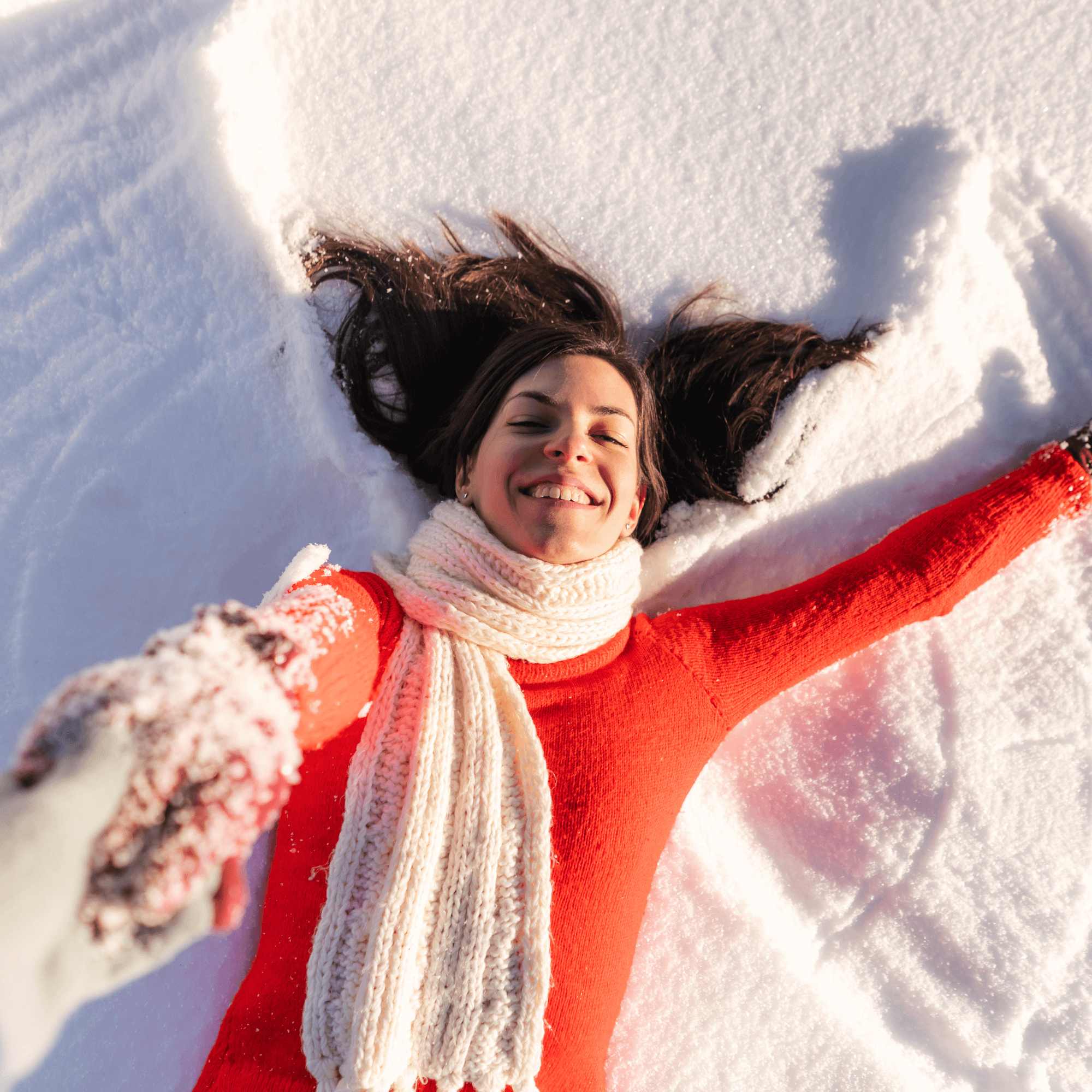 Smiling woman in red sweater and white scarf lying in snow enjoying winter outdoors