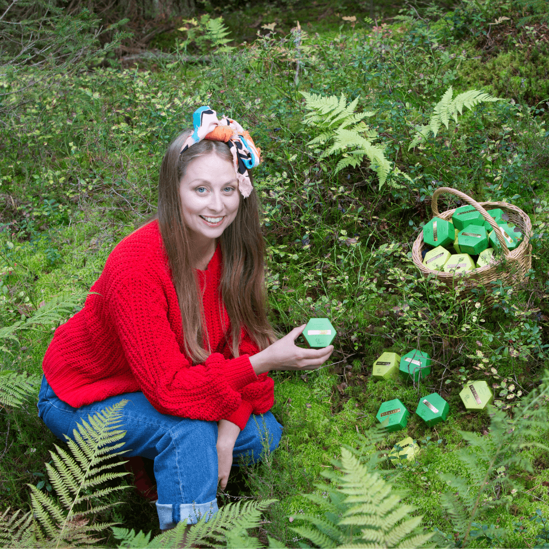 Woman in red sweater holding natural skincare product outdoors with basket of green Luonkos skincare boxes in forest setting, Vuoden luontoyritys award winner 2023.