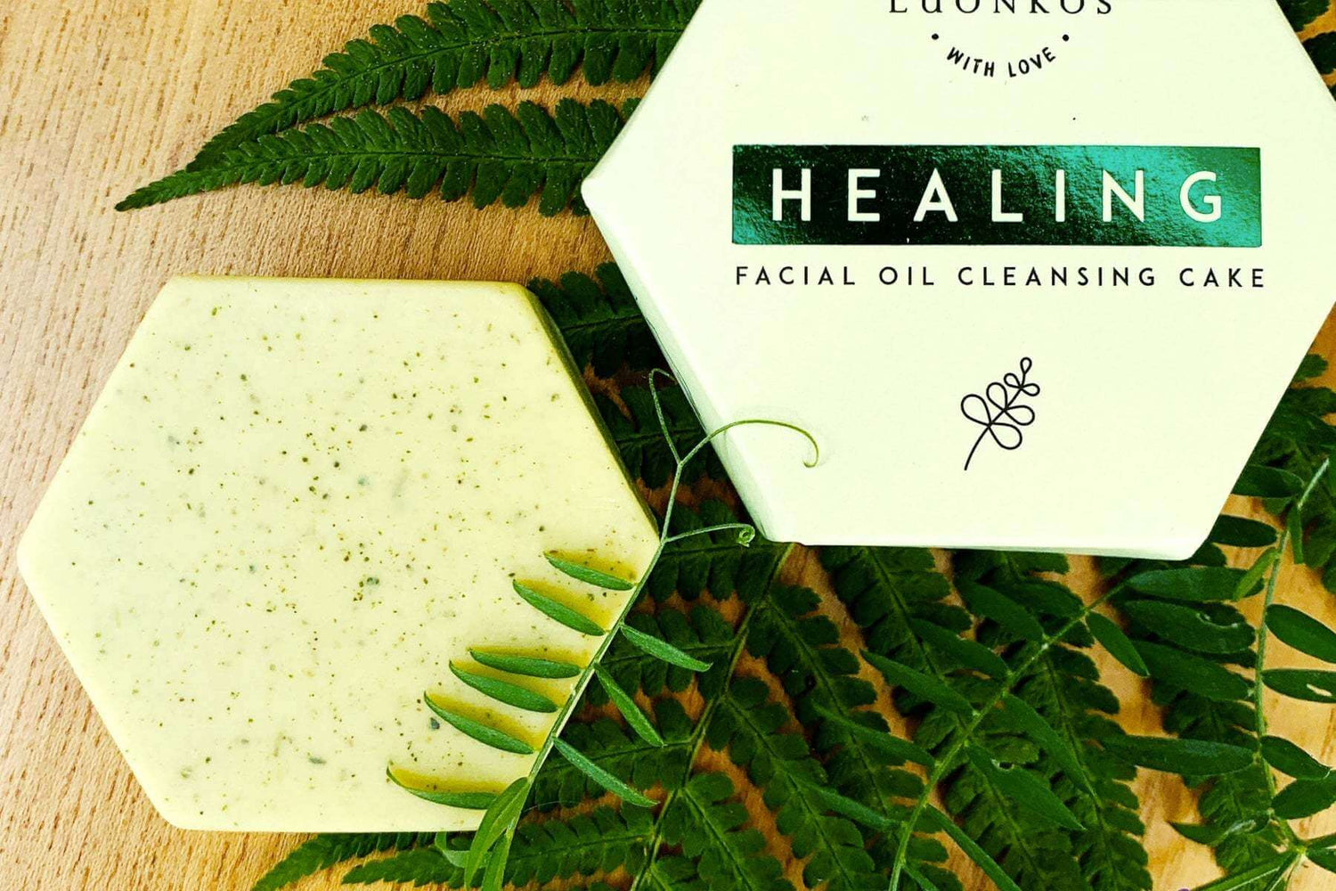 Hexagonal Luonkos healing facial oil cleansing cake with natural fern leaves and white eco-friendly packaging on wooden surface