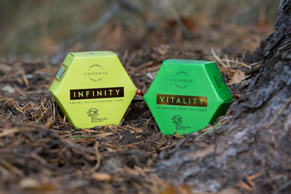 Luonkos natural skincare products Infinity facial oil cleansing cake and Vitality balancing body oil cake on forest floor promoting luontoaltistus huolehtii terveydestä.