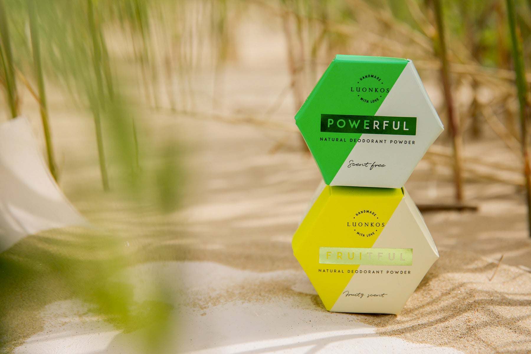 Luonkos Powerful and Fruitful natural deodorant powders stacked on sandy beach background