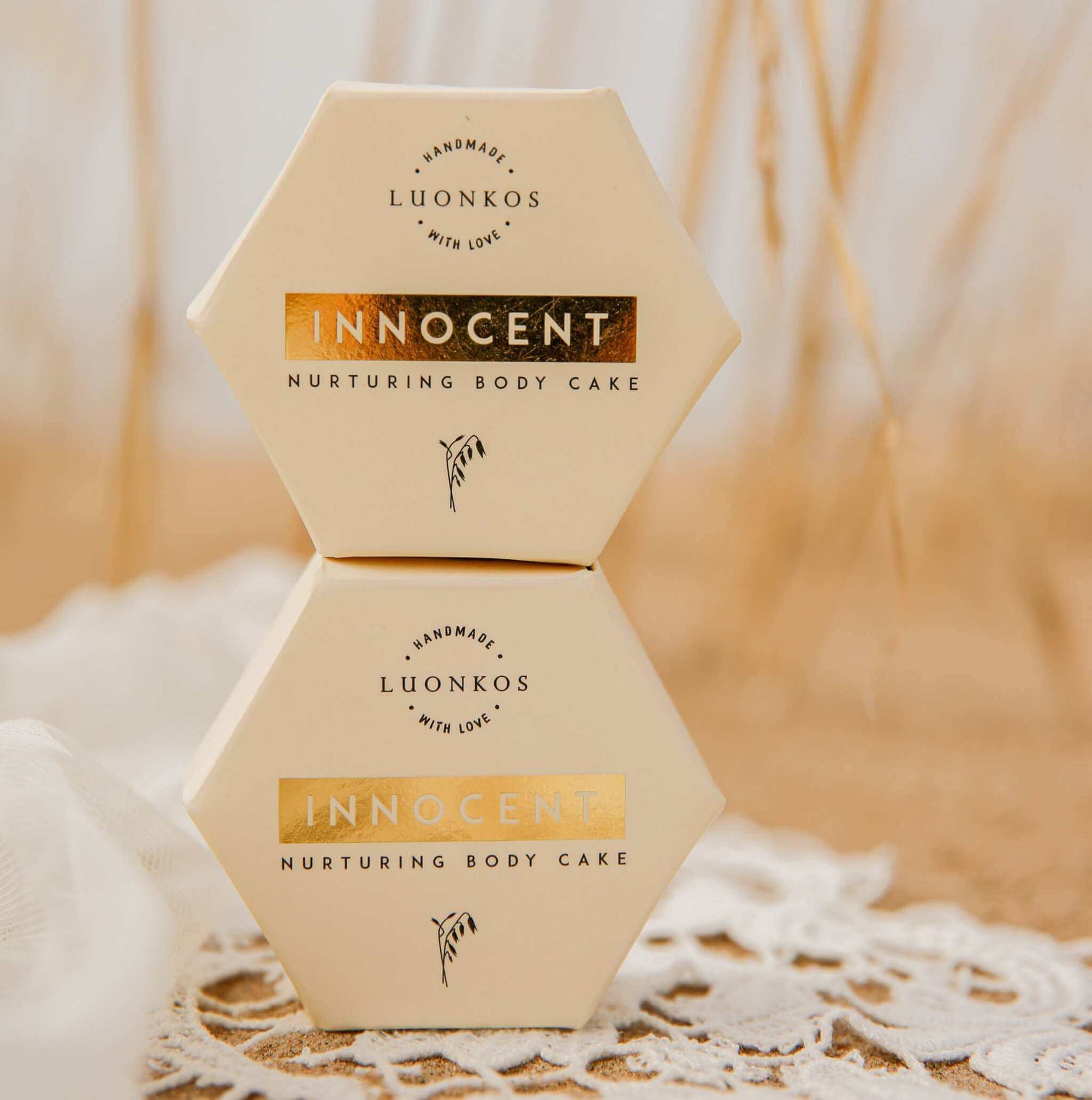 Luonkos Innocent nurturing body cake natural skincare hexagon packaging stacked on lace fabric highlighting vartalon ihonhoidon tärkeys.