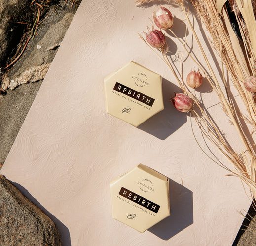 Two hexagonal Luonkos Rebirth facial oil cleansing cakes on a textured beige surface with dried flowers and natural elements nearby, showcasing Luonkosin suosituimmat tuotteet natural skincare.