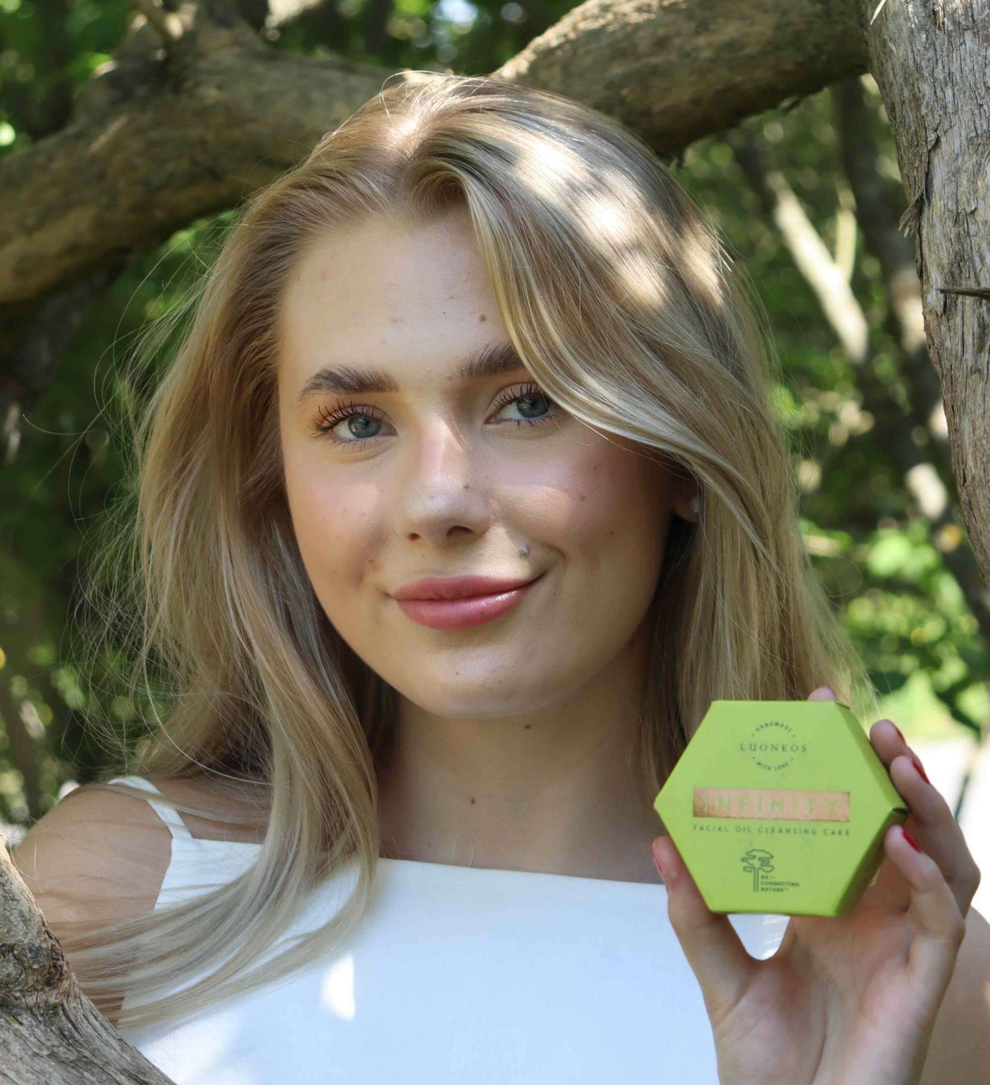 Young woman holding a hexagonal green soap box outdoors promoting the importance of oil cleansing for healthy summer skin