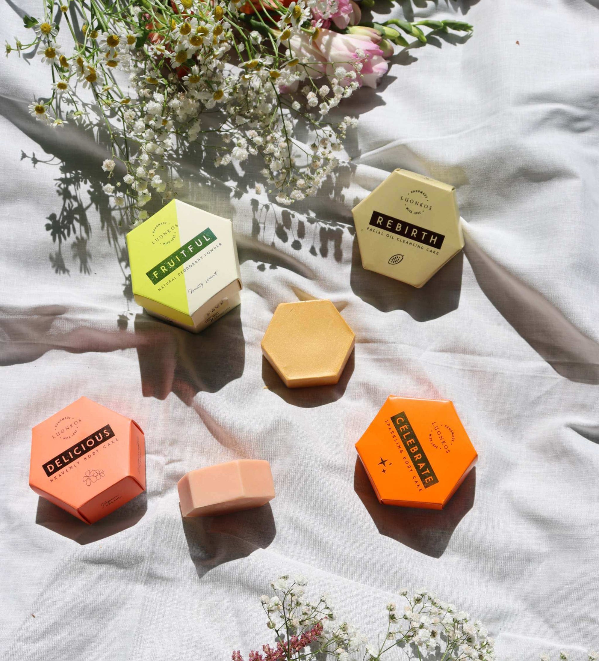 Hexagonal skincare bars in pastel and bright colors on white fabric with small flowers, promoting kevään ihonhoito (spring skincare) products